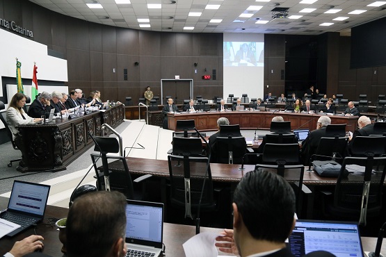Homens e mulheres sentados em bancada semicircular de madeira voltados para mesa de autoridades em sessão do Tribunal de Justiça.