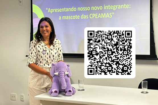 Mulher, que apoia um elefante roxo de pelúcia em cima de uma mesa branca, posa para a foto. No lado direito da imagem está um QR code. Também existe atrás da mulher uma projeção em uma tela que diz em letras amarelas “Apresentando nosso novo integrante: a mascote das CPEAMAS”.