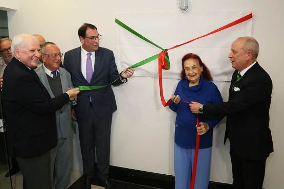 Quatro homens e uma mulher seguram uma fita verde e vermelha que envolve um pano retangular preso em uma parede.