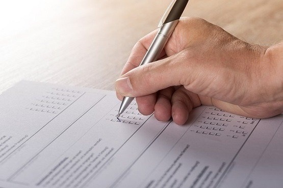 Imagem de uma folha de papel, sobre uma mesa sendo assinado por uma mão com uma caneta.