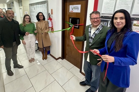 Cinco pessoas, sendo 2  homens e 3 mulheres, seguram uma fita verde e vermelha que enlaçam a porta de uma sala