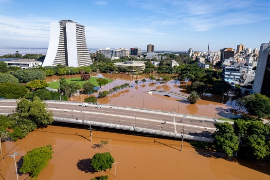 Imagem aérea de uma das cidades afetadas pelas fortes chuvas no estado do Rio Grande do Sul. A imagem mostra alguns prédios, árvores e um viaduto.