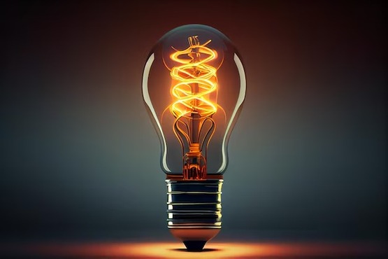 A imagem mostra uma lâmpada incandescente acesa, com um filamento em espiral brilhando em um tom alaranjado. A lâmpada está posicionada horizontalmente contra um fundo escuro, que realça o brilho do filamento. À esquerda da imagem, há uma barra lateral com texto, mas o foco principal é a lâmpada iluminada.