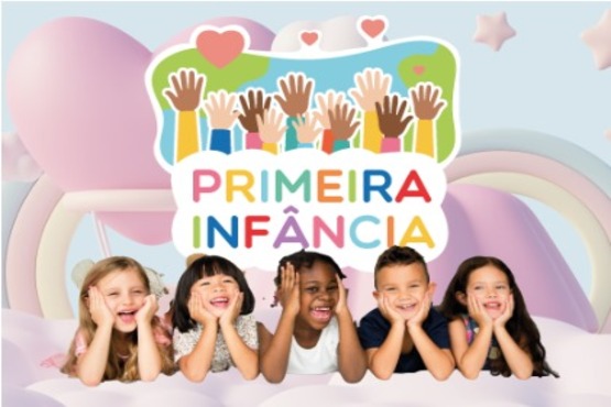 A imagem mostra cinco crianças deitadas de bruços, apoiadas nos cotovelos e sorrindo. Elas estão em um ambiente colorido e alegre, com um fundo de uma montagem que parece remeter a nuvens e formas suaves. Acima das crianças, há um desenho de várias mãos levantadas de diferentes cores, simbolizando diversidade. No centro da imagem, está escrito "Primeira Infância" em letras coloridas.