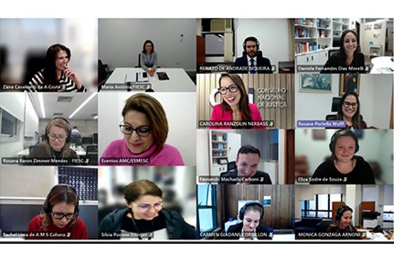 A imagem mostra uma captura de tela de uma videoconferência com várias pessoas em suas respectivas janelas de vídeo. Há um total de 12 participantes visíveis, distribuídos em uma grade de 3 colunas e 4 linhas. Cada pessoa está em um ambiente diferente, a maioria em escritórios ou salas de casa. Algumas pessoas estão sorrindo, outras parecem estar falando ou ouvindo atentamente.