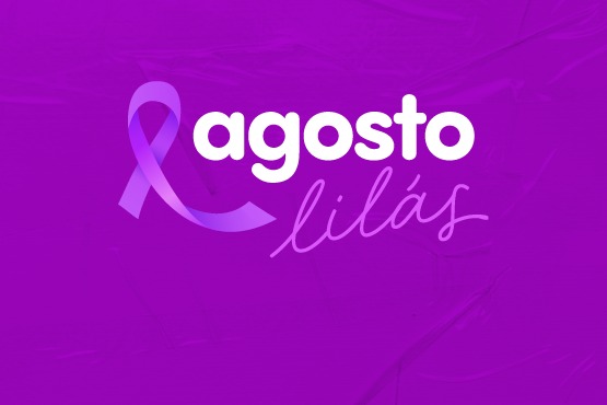 A imagem tem um fundo roxo e contém a frase "agosto lilás". A palavra "agosto" está escrita em letras brancas e em negrito, enquanto "lilás" está em uma fonte cursiva e na cor lilás. À esquerda da palavra "agosto", há um laço na cor lilás, que é um símbolo frequentemente usado em campanhas de conscientização.