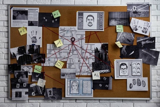 A imagem mostra um quadro de cortiça típico de investigações policiais, com várias fotos, documentos e notas adesivas conectadas por fios vermelhos. No centro, há um mapa com várias linhas vermelhas convergindo para um ponto. Ao redor do mapa, há fotos de pessoas, impressões digitais, uma marca de mão, e várias outras imagens relacionadas à investigação. As notas adesivas têm números e datas, como "24 May" e "#4". Parece ser uma representação de uma investigação complexa, possivelmente de um crime.