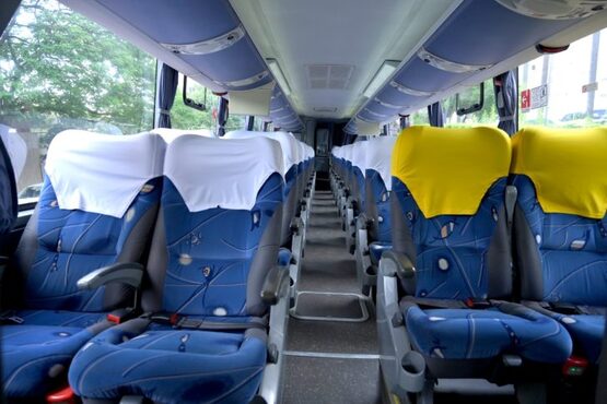 A imagem mostra o interior de um ônibus de viagem, Dois assentos na direita estão com capas amarelas e os outros com capas brancas.