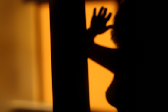 A imagem mostra a silhueta de uma pessoa contra um fundo iluminado de cor amarela ou laranja. A pessoa está com um braço levantado. A silhueta é escura e não permite ver detalhes do rosto ou das roupas da pessoa.