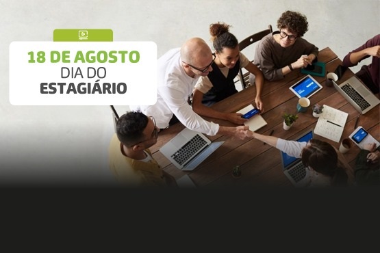 A imagem celebra o "Dia do Estagiário", que é comemorado em 18 de agosto. No lado esquerdo da imagem, há um texto em um fundo branco e verde que diz "18 de agosto Dia do Estagiário". No lado direito, há uma foto de um grupo de pessoas sentadas ao redor de uma mesa de madeira. Elas estão usando laptops e tablets, e duas pessoas estão apertando as mãos, sugerindo um ambiente de trabalho colaborativo e amigável.