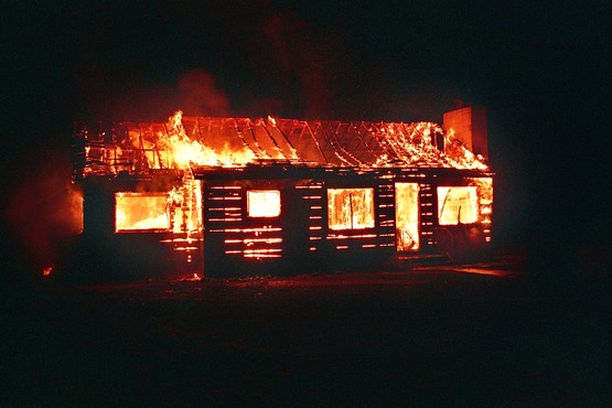 A imagem mostra uma casa de madeira pegando fogo.