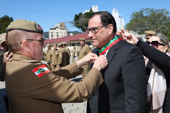 Foto horizontal: Francisco Oliveira Neto recebe homenagem militar em cerimônia ao ar livre sob céu azul.