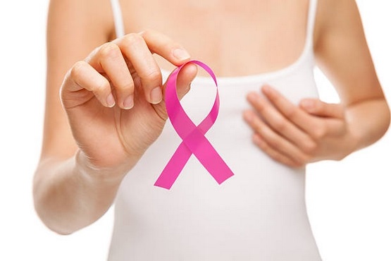 A imagem mostra uma pessoa vestindo uma regata branca, segurando um laço rosa com a mão direita. O laço rosa é um símbolo internacional da luta contra o câncer de mama. A mão esquerda da pessoa está posicionada sobre o peito, sugerindo um gesto de conscientização ou autoexame. O fundo da imagem é branco e neutro.
