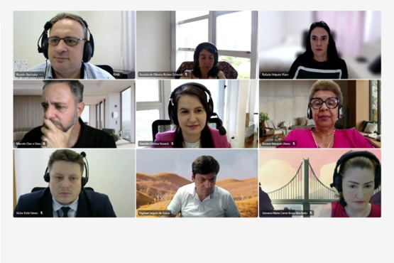 A imagem mostra uma captura de tela de uma reunião virtual com nove participantes, cada um em sua própria janela. Os participantes exibem diversas expressões e ambientes; alguns parecem estar em escritórios com livros e decorações ao fundo, enquanto outros têm fundos mais simples ou virtuais, como paisagens ou pontes. Há uma mistura de homens e mulheres, alguns vestindo trajes formais como ternos, enquanto outros estão mais casuais. Cada janela de vídeo também mostra o nome do participante, sugerindo um ambiente profissional ou corporativo. A reunião parece ser séria, refletindo uma discussão importante ou um encontro formal de trabalho.