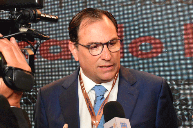 Foto horizontal: desembargador Francisco Oliveira Neto concede entrevista, microfones à frente, ambiente de evento, tons escuros.