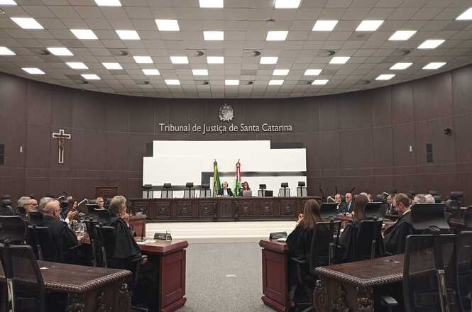 A imagem mostra a sala do Tribunal do Júri no Tribunal de Justiça de Santa Catarina. O ambiente é amplo, com cadeiras e mesas dispostas em semicírculo, e ao fundo há uma bancada elevada com bandeiras atrás.