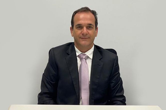 A imagem mostra o Juiz Emanuel Schenkel do Amaral e Silva, vestindo um terno preto, camisa branca e gravata clara, em um ambiente com fundo neutro.