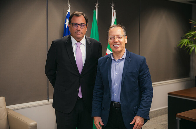 Foto horizontal: desembargadores Francisco Oliveira Neto e Carlos França posam juntos, bandeiras ao fundo, ambiente institucional.