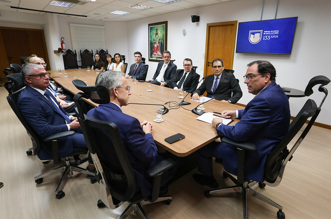 A imagem mostra o Salão Nobre do gabinete da presidência do TJSC. No centro da sala há uma mesa oval, várias pessoas estão sentadas em volta dela, incluindo o desembargador Francisco Oliveira Neto e o prefeito de Blumenau.