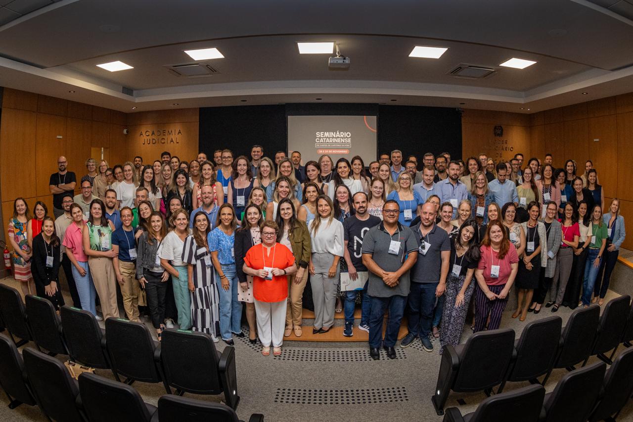 A imagem mostra um auditório onde ocorreu o Seminário Catarinense de Chefes de Cartório do PJSC. No palco um homem está falando no microfone, enquanto a plateia está sentada em cadeiras pretas.