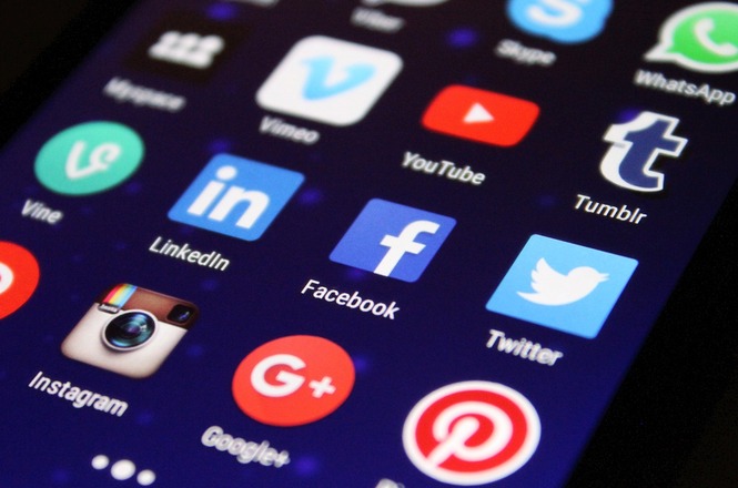 A imagem mostra a tela de um celular com vários ícones de aplicativos de redes sociais. O fundo da tela é escuro.