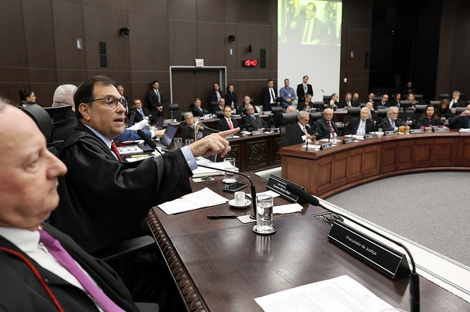 A imagem mostra uma sessão no Tribunal de Justiça de Santa Catarina. Na imagem o residente desembargador Francisco Oliveira Neto está de toga, falando e apontando com o dedo. Ao fundo, há outros magistrados e servidores do tribunal, bem como uma projeção na parede.