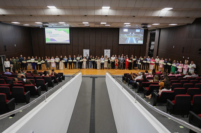 A imagem mostra o Pleno do Tribunal de Justiça de Santa Catarina (TJSC) durante um evento. Um grupo de pessoas está alinhado na frente do auditório, segurados recursos do PJSC Mais Social, enquanto o público está sentado em cadeiras vermelhas e pretas.
