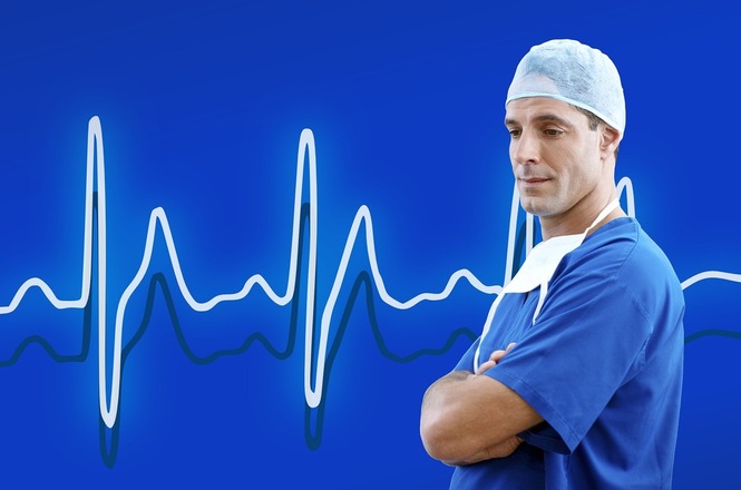 A imagem mostra um profissional de saúde usando uniforme azul e uma touca cirúrgica. Ele está de braços cruzados, e ao fundo, há um gráfico de linha semelhante a um eletrocardiograma, em uma cor azul clara sobre um fundo azul mais escuro.