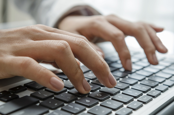 A imagem mostra duas mãos digitando em um teclado de computador. As mãos estão em uma posição típica de digitação, com os dedos pressionando diferentes teclas. O teclado é preto com letras brancas. A imagem sugere uma atividade de trabalho ou estudo relacionada ao uso do computador.