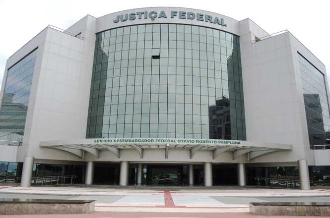 Prédio moderno com fachada de vidro curvada e estrutura em concreto. No topo, está escrito "JUSTIÇA FEDERAL" em letras grandes. Abaixo, sobre a entrada principal, há uma inscrição que diz "EDIFÍCIO DESEMBARGADOR FEDERAL OTÁVIO ROBERTO PAMPLONA". A entrada é ampla, com várias colunas sustentando uma marquise. O edifício tem um design simétrico e imponente.