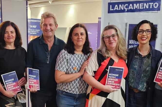 A imagem mostra cinco pessoas posando para uma foto em um evento de lançamento. Estão segurando livros com uma capa que parece ser a mesma para todos. Atrás deles, há um cartaz ou banner com a palavra "LANÇAMENTO" escrita em destaque. As pessoas estão sorrindo e parecem participar de uma celebração relacionada aos livros que estão segurando.