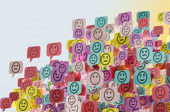 A imagem mostra muitos balões de fala coloridos, cada um contendo um rosto de emoji com diferentes expressões faciais. Os balões estão em várias cores, como vermelho, amarelo, azul e roxo, e apresentam uma variedade de emoções, incluindo felicidade, tristeza e neutralidade. Eles estão sobrepostos e espalhados de forma caótica, criando uma sensação de mistura de sentimentos e comunicação.