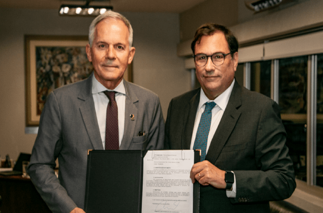 Foto horizontal: Francisco Oliveira Neto exibe documento com autoridade, em ato oficial, ambiente interno, tons neutros.