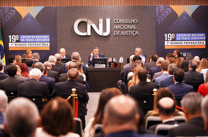 A imagem mostra uma reunião do Conselho Nacional de Justiça (CNJ). Está ocorrendo o "19º Encontro Nacional do Poder Judiciário" e a "1ª Reunião Preparatória", datada de 7 de maio de 2025. Um grande número de pessoas está presente, todas voltadas para um painel onde algumas pessoas estão discursando. Ao fundo, há uma grande placa com o logotipo do CNJ. A imagem transmite um ambiente formal e profissional.