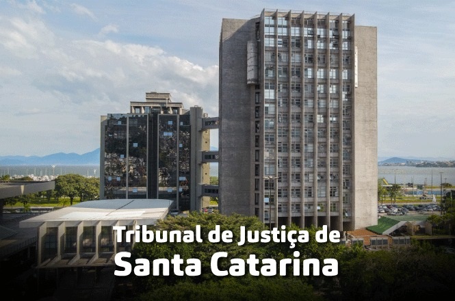 A imagem mostra o Tribunal de Justiça de Santa Catarina, localizado em Florianópolis. O edifício é composto por estruturas modernas e altas, com várias janelas. Ao fundo, é possível ver uma paisagem com árvores e o céu parcialmente nublado. A foto tem a legenda "Tribunal de Justiça de Santa Catarina" na parte inferior da imagem.