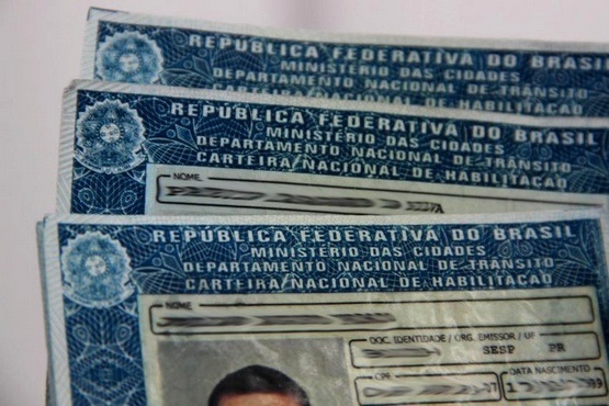 A imagem mostra três Carteiras Nacionais de Habilitação (CNHs) brasileiras empilhadas. No topo de cada documento, está escrito "República Federativa do Brasil" e "Carteira Nacional de Habilitação". A parte superior da foto revela o layout e elementos de segurança típicos desses documentos oficiais. Num dos documentos, é possível ver parcialmente uma foto de uma pessoa.
