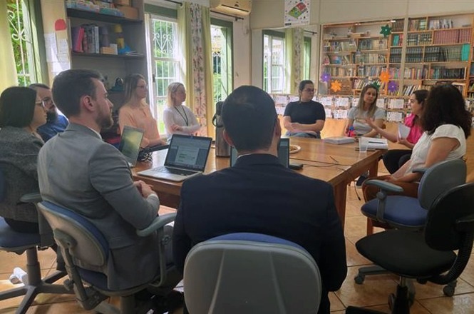 A imagem mostra um painel de discussão com cinco homens sentados em poltronas em um auditório. Eles estão em um palco discutindo, e um dos homens está falando ao microfone. O público está sentado em cadeiras à frente, assistindo à conversa. Todos os palestrantes estão vestindo ternos formais, e há mesas com jarras de água entre eles. É um ambiente profissional, provavelmente em um evento ou conferência.