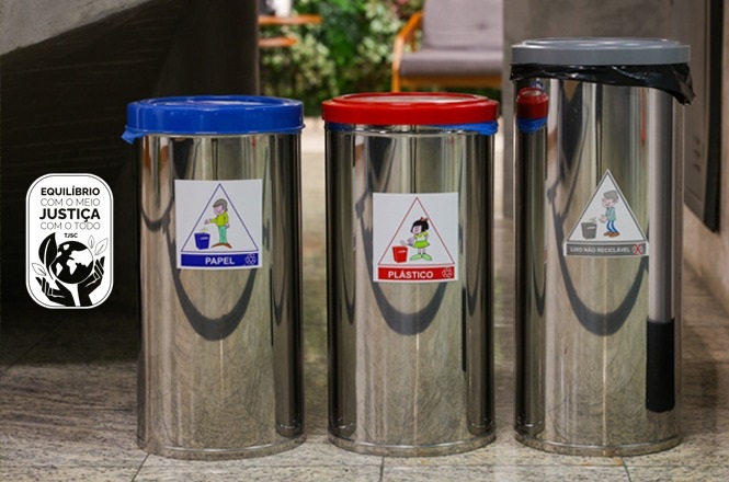 A imagem mostra três lixeiras de metal, cada uma com uma tampa de cor diferente: azul, vermelha e cinza. A lixeira azul é para papel, a vermelha para plástico, e a cinza para lixo não reciclável. Cada lixeira possui um adesivo ilustrativo correspondente ao tipo de resíduo que deve ser depositado nela. Ao lado das lixeiras, há um adesivo com a frase "Equilíbrio com o meio, justiça com o todo" e um desenho de um globo terrestre segurado por mãos.