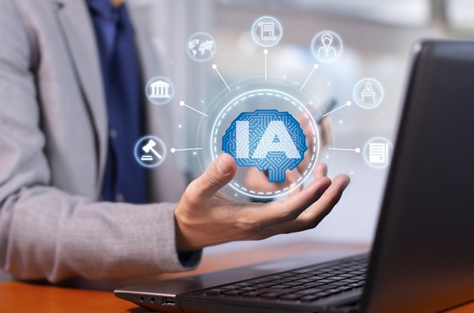 Na imagem, há uma pessoa usando um computador portátil. A mão da pessoa está estendida e sobre ela há uma ilustração digital de um cérebro com a sigla "IA" no centro, que representa "Inteligência Artificial". Ao redor do cérebro, existem vários ícones conectados, simbolizando diferentes campos ou aplicações, como justiça, educação, saúde e negócios. Ao fundo, o ambiente parece ser um escritório ou local de trabalho.