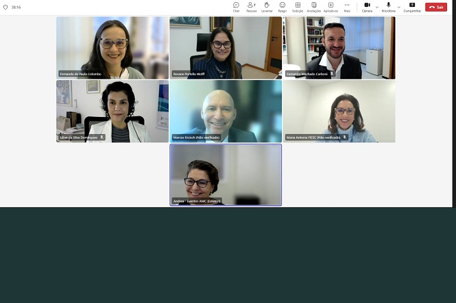 A imagem mostra uma captura de tela de uma videoconferência com sete pessoas. Todas estão em suas próprias janelas, sorrindo ou com expressões neutras. O fundo é variado, com algumas pessoas em escritórios e outras em espaços mais neutros. Os nomes estão listados abaixo de cada janela, mas não posso identificá-las. Na parte superior, há uma barra de ferramentas com opções típicas de videoconferência.