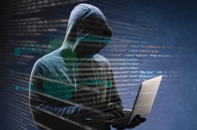 A imagem mostra uma pessoa com um capuz escuro mexendo em um laptop. O ambiente é escuro, e há códigos de computador e gráficos projetados ao redor, sugerindo um tema de hacking ou segurança cibernética.