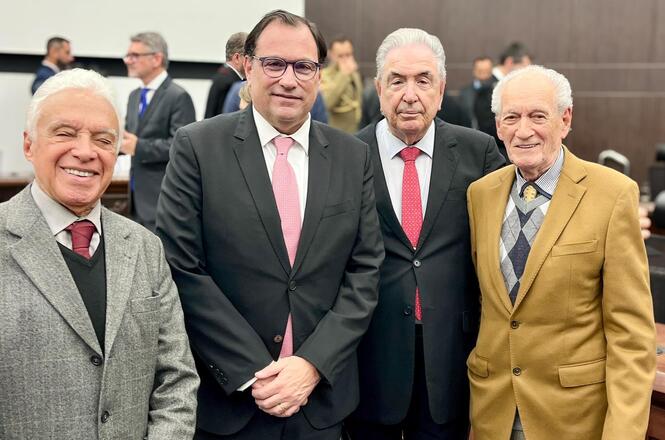 Foto horizontal: Francisco Oliveira Neto posa com autoridades em evento, grupo sorridente, ambiente interno, tons neutros.