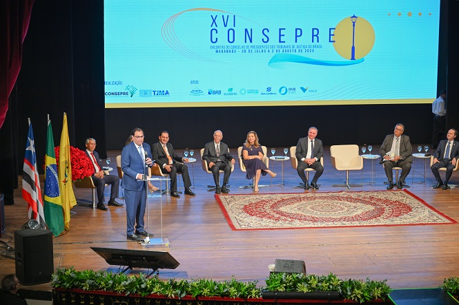 A imagem mostra um homem de terno falando em um púlpito com microfone em uma conferência ou evento formal. Atrás dele, há uma tela grande com o logotipo e informações do "XIX CONSEPRE", que parece ser um encontro de presidentes dos tribunais de justiça do Brasil, ocorrido em 2023. No palco, há várias pessoas sentadas em um painel, todas em trajes formais.