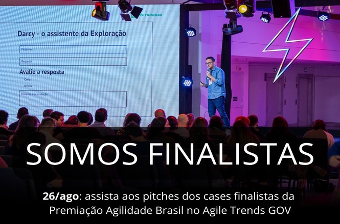 A imagem apresenta uma cena em um ambiente de conferência ou evento, onde há uma apresentação ocorrendo. No primeiro plano, há uma plateia sentada, composta por várias pessoas que parecem estar assistindo atentamente à apresentação.
