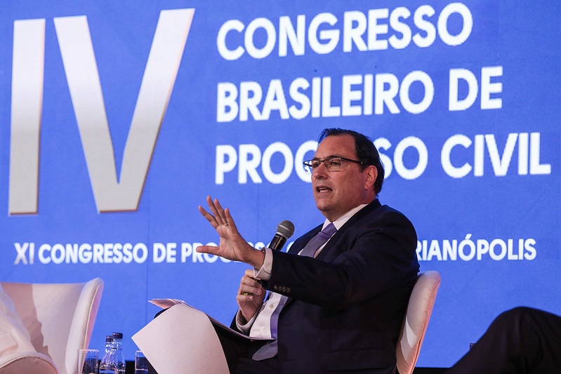 O Presidente do TJSC fala ao microfone durante a conferência, com papéis em mãos. Ao fundo, a tela mostra “IV Congresso Brasileiro de Progresso Civil” e “XI Congresso de Progresso Civil em Florianópolis”.