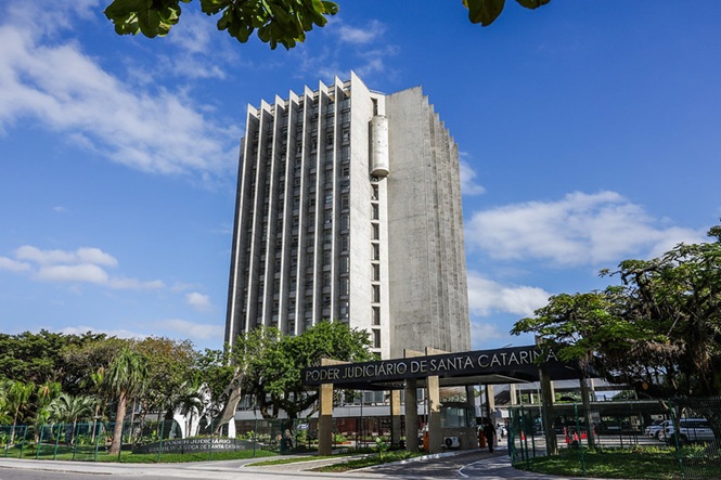 A imagem mostra o edifício do Tribunal de Justiça de Santa Catarina, com arquitetura moderna e imponente, cercado por área ajardinada com árvores.
