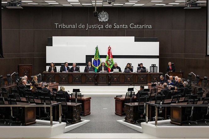Sessão solene no Tribunal de Justiça de Santa Catarina, com público em semicírculo e juízes na bancada elevada, sob as bandeiras do Brasil e do estado, em clima formal e institucional.
