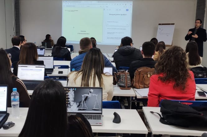 Sala de aula moderna com estudantes atentos usando laptops, acompanhando o instrutor junto ao quadro branco. O ambiente é profissional e focado, marcado por concentração e interesse.
