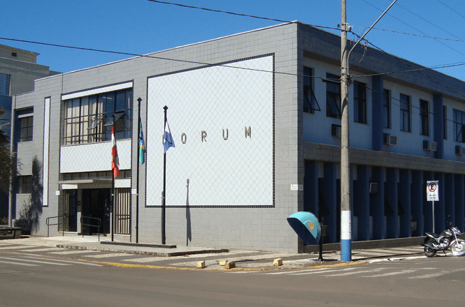 A imagem mostra um edifício moderno identificado como “Fórum” em uma esquina, com calçadas, poste de iluminação e uma moto estacionada em frente.