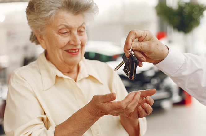 A imagem mostra uma senhora sorridente recebendo as chaves de um carro em um ambiente interno, possivelmente uma concessionária, transmitindo alegria e satisfação.